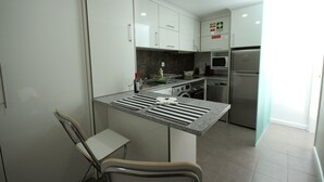 Una cocina moderna con armarios blancos, horno empotrado, microondas y refrigerador de acero inoxidable.