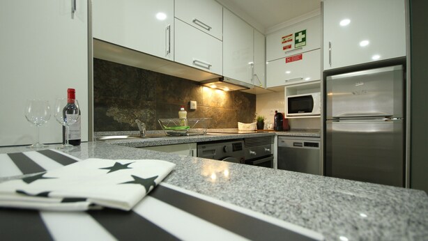 Una cocina moderna con gabinetes blancos, encimera de granito, refrigerador de acero inoxidable y un microondas.