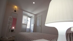 Un dormitorio con cama, mesita de noche, lámpara, armario y ventana con persianas.