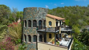 Un bâtiment en pierre de deux étages, doté d’un balcon et entouré d’une végétation luxuriante.