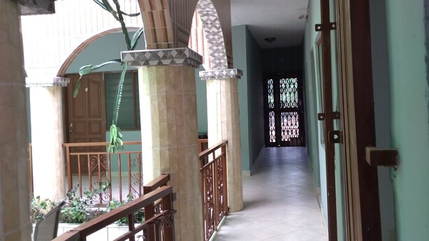 Un corridoio con pavimento piastrellato, una scala con ringhiera in metallo e vista su una porta con inferriata decorativa.