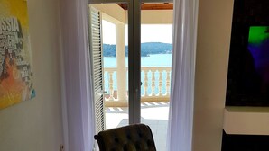 Une pièce avec un plancher en bois, un fauteuil en cuir, un tableau et une vue sur un balcon doté d’une balustrade.