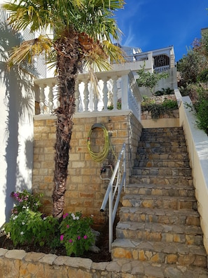 Stunning residential building with a stone staircase, balcony, and lush greenery.