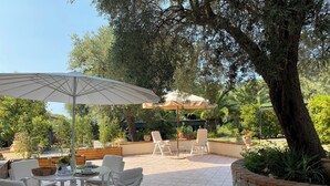 Un espace extérieur aménagé en terrasse, avec une table ronde, des chaises blanches et un grand parasol.