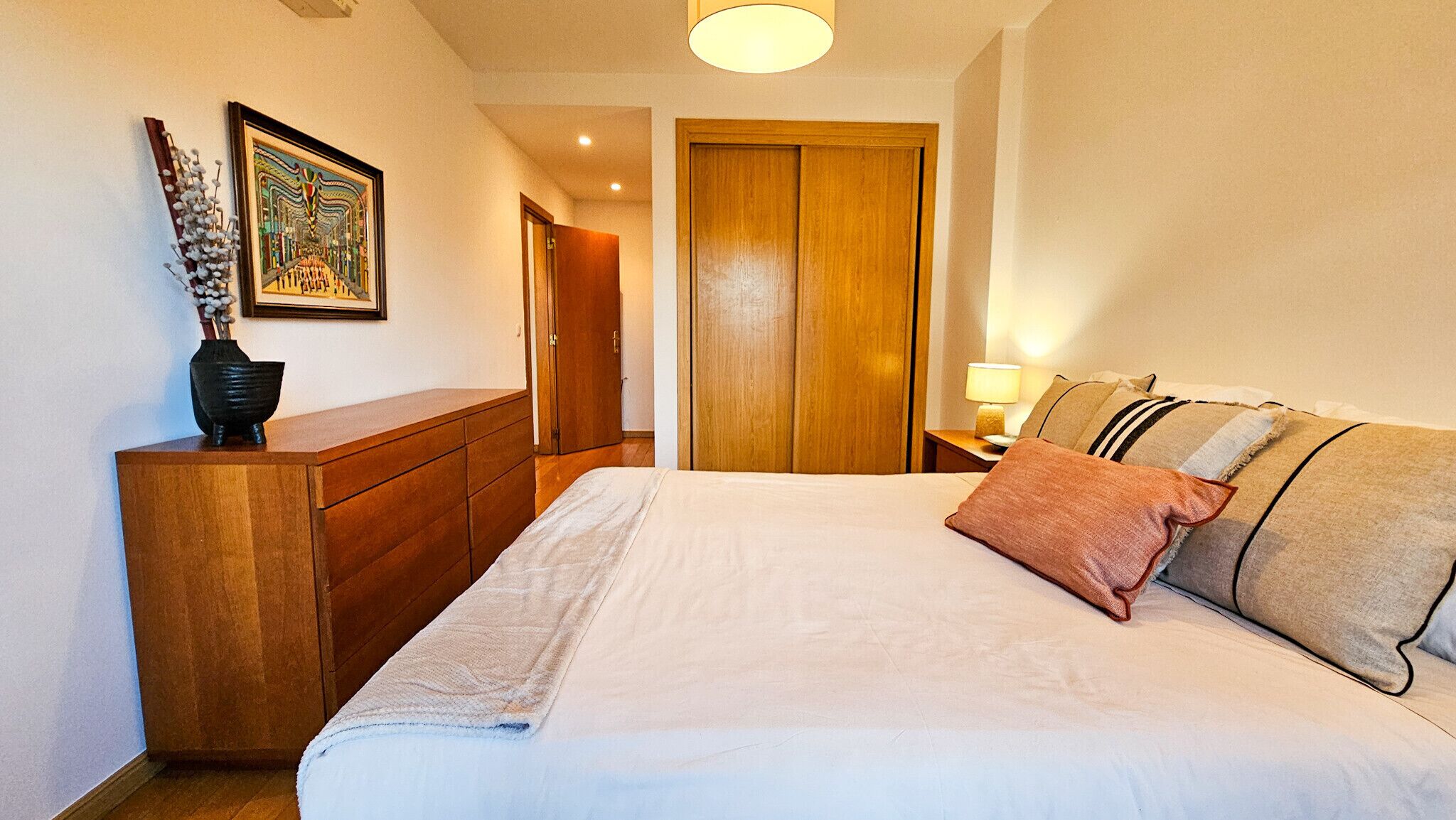 A bedroom with a bed, a dresser, a wooden door, and a nightstand with a lamp.