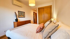 Une chambre à coucher comprenant un lit, une commode, un tableau encadré, une porte en bois et un appareil de climatisation.