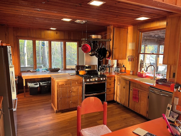 A wooden cabin kitchen with a stove, oven, and hanging pots.
