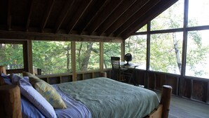 Een slaapkamer in een houten hutje, met een bed, een bureau en een stoel.