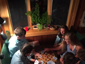Un groupe de personnes joue à un jeu de cartes autour d’une table en bois, avec une fenêtre en arrière-plan.