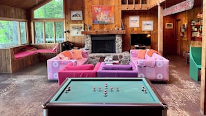 Een knus interieur van een chalet, met een pooltafel, houten meubels, een open haard en grote ramen.