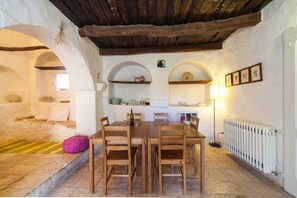 Ein rustikaler Essbereich mit Steinboden, Holztisch und Stühlen. Es gibt rundbogige Nischen mit Regalen über dem Tisch.