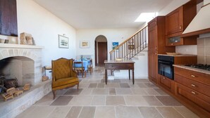 Uma sala de estar ampla, com lareira, mesa de jantar e escada que dá para uma cozinha.