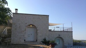 Um edifício de pedra com porta branca, uma pequena varanda e área de piscina.