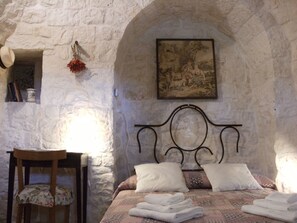 Ein Schlafzimmer mit Steinswand, einem Bett mit weißen Leinen, einem Holzstuhl und einem Gemälde.