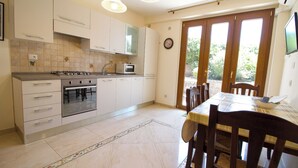 A kitchen with white cabinets, a stove, a microwave, and a dining table with chairs. - Apartment with Garden View (Trecastagni)