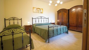 A bedroom with two metal-framed beds, a wooden wardrobe, a nightstand with a lamp, and a painting on the wall. - Apartment with Garden View (Trecastagni)