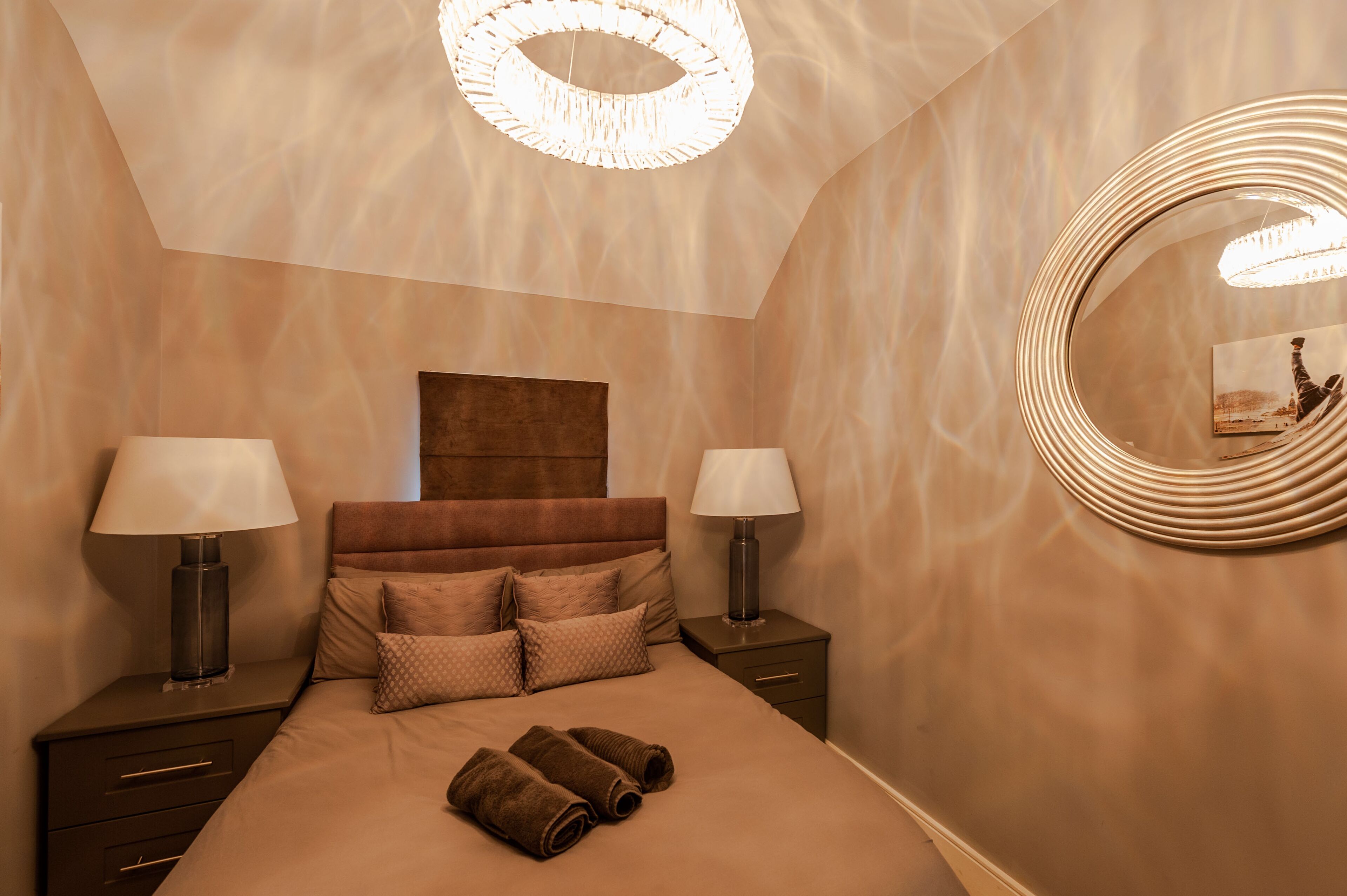 Camera d'albergo con un letto grande, due comodini con lampade, uno specchio rotondo e un lampadario.