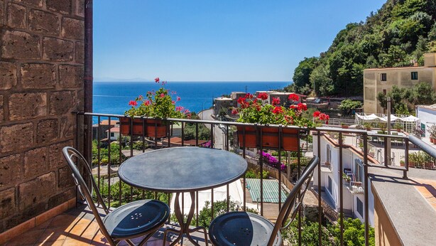 A balcony with a table and chairs, overlooking a coastal area with buildings and greenery. - La Rotonda Deluxe Apartment (Nerano)
