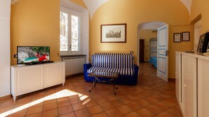 A living room with a sofa, TV, and a small table. There is a door leading to another room. - La Rotonda Deluxe Apartment (Nerano)