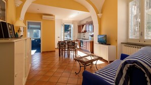 A spacious living area with a dining table, kitchen, and a large window providing a view of the outdoors. - La Rotonda Deluxe Apartment (Nerano)