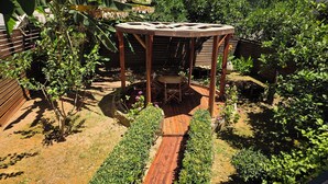A wooden pergola with a table and chairs, surrounded by a garden with various plants and a wooden fence. - Minoa Downtown  Garden villa (Κουνουπιδιανά)