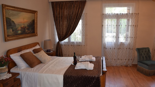 A neatly made bed with a bottle and glasses, a chair, and a painting on the wall. - Minoa Downtown  Garden villa (Κουνουπιδιανά)