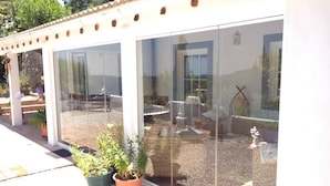 En moderne bygning med store glasruder, en terrasse med plantekasser og udendørs møbler.