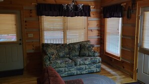 A log cabin interior with a patterned sofa, wooden walls, and a door with a window. - Cozy Log Cabin Getaway Waynesville, Smokey Mountains, Blue ridge Parkway (Canton)