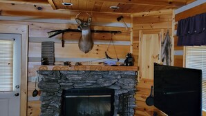 A log cabin interior with a stone fireplace, mounted deer head, and hunting equipment. - Cozy Log Cabin Getaway Waynesville, Smokey Mountains, Blue ridge Parkway (Canton)