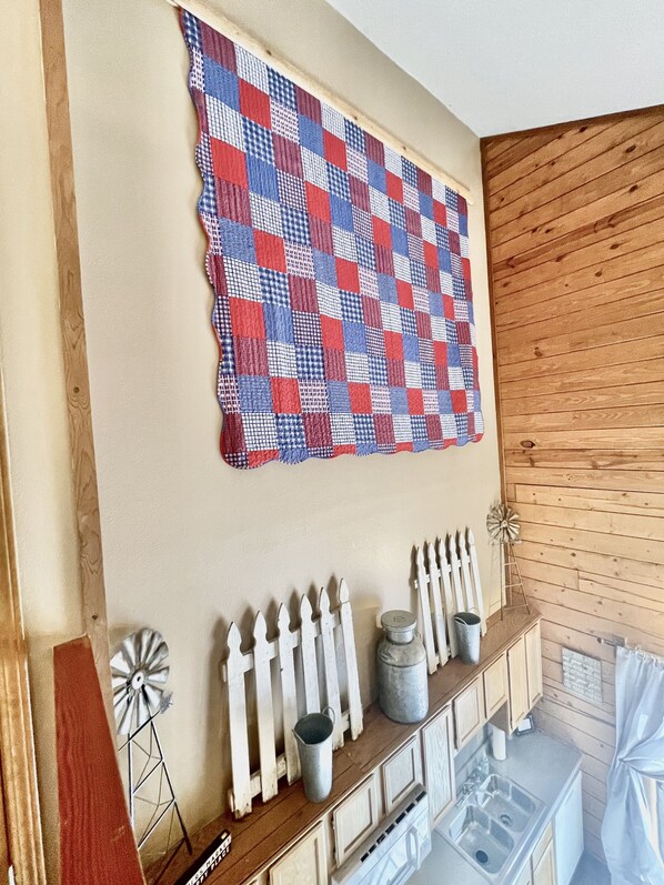 A room with a quilted wall hanging, wooden wall paneling, a white picket fence, metal buckets, and a windmill decoration.