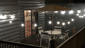 An outdoor dining area with a round table and chairs, string lights, and a wooden deck.