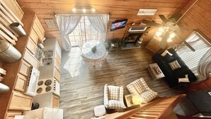A cozy cabin-style room with a wooden interior, a dining area with a table and chairs, a sofa, and a staircase.