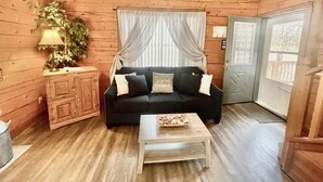 A cozy cabin-style room with a wooden interior, a black sofa with cushions, a small wooden table, and a potted plant.