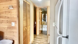 A wooden interior with a kitchen area, including a refrigerator, wooden cabinets, and a hallway leading to a bathroom.