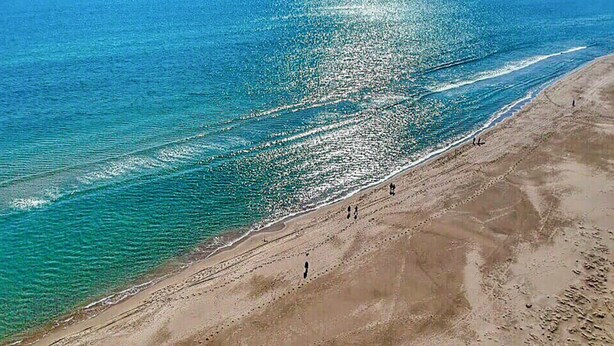 A beach with clear water, a sandy shore, and a few people walking.