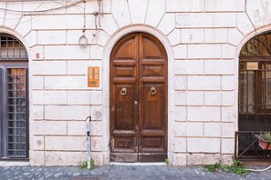 Um edifício com uma grande porta dupla de madeira, uma pequena janela com grade de metal e um vaso com planta à direita.