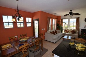Uma área de refeições com uma mesa posta para quatro pessoas, um sofá branco e um ventilador de teto.