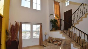 Un salón amplio con sofá, una escalera y vistas a través de un ventanal grande.