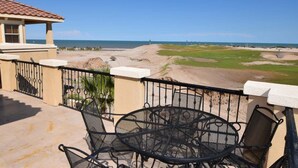Un balcón con mesa y sillas, con vistas a un campo de golf y al océano.