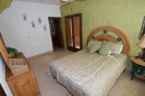 Quarto com cama, cabeceira de madeira, mesa pequena e porta.