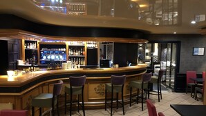 Un espace bar doté d’un comptoir incurvé, de plusieurs tabourets et d’une variété de bouteilles et de verres disposés sur des étagères.