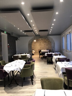 A restaurant with multiple tables and chairs, a stone wall in the background, and a modern ceiling design. - Hotel des Voyageurs (Le Rouget-Pers)