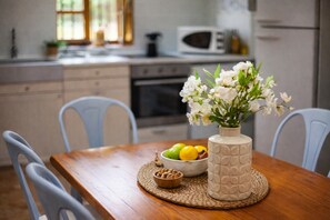 Een houten eettafel met een geweven placemat, een schaal met fruit en een vaas met witte bloemen.