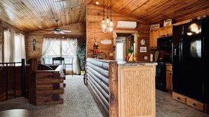Une cuisine chaleureuse, aménagée dans le style d’un chalet, avec des murs en bois et un îlot central, comprenant un réfrigérateur, une cuisinière et un coin repas.