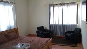 Une chambre à coucher avec un lit, deux chaises, un ventilateur de plafond et une fenêtre avec des rideaux.