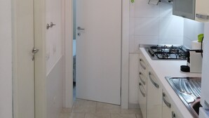 Une cuisine étroite avec des meubles blancs, une cuisinière à gaz et un climatiseur fixé au mur.