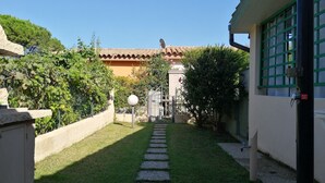Un chemin menant à un bâtiment doté d’un toit en tuiles, entouré de verdure et d’une clôture.