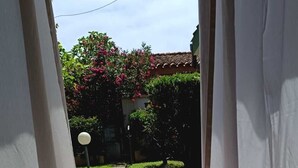 Une vue à travers une porte donnant sur une cour intérieure avec un chemin de pierre, de l’herbe verte et un arbre aux fleurs roses.