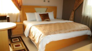 A neatly arranged bedroom with a bed, bedside tables, a round table, and patterned curtains. - Frankville Hotel (Abuja)