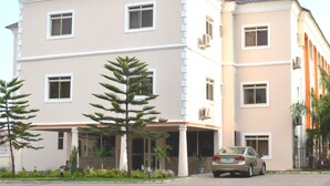 A multi-story hotel with a beige facade, multiple windows, and a covered entrance area with palm trees. - Frankville Hotel (Abuja)